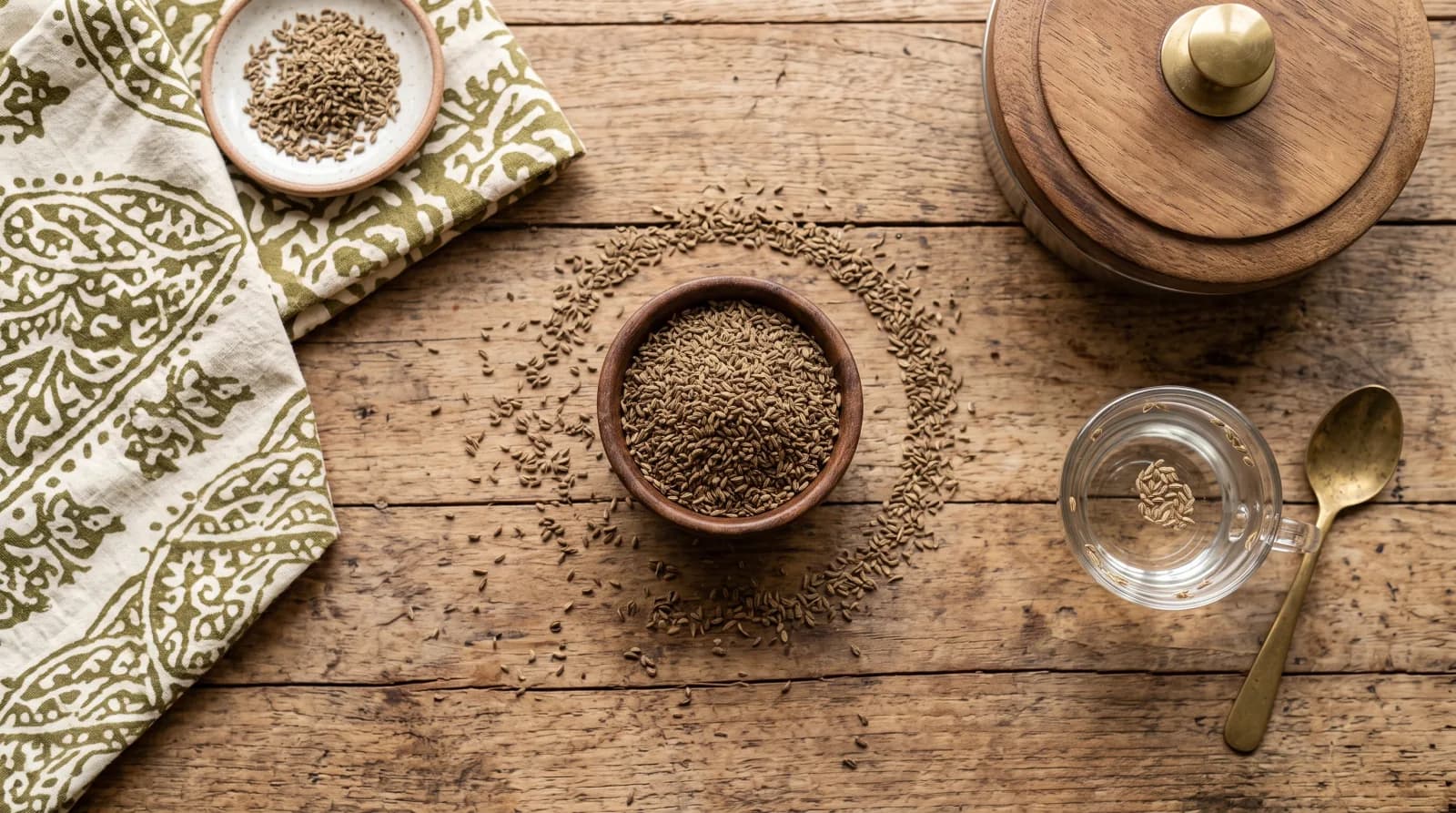 A small bowl of ajwain (carom seeds) on a wooden table, styled with a traditional masala box